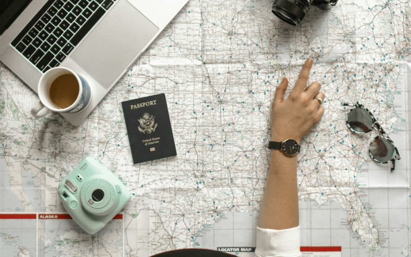 Hand on map with camera, passport, laptop, and coffee, perfect for travel planning inspiration.